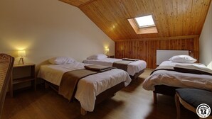 Ein gemütliches Schlafzimmer im Dachgeschoss mit drei Betten, Holzbalkendecke und einem Dachfenster.