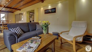 Ein gemütliches Wohnzimmer mit grauem Sofa, einem Holztisch mit Zeitschriften, einem weißen Sessel und einem Blumenstrauß mit gelben Blüten.