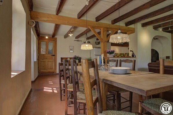 A dining area with a wooden table and chairs, a chandelier, and a kitchen in the background. - Le Tilleret - Chezery-forens (CHEZERY-FORENS)