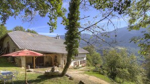 A rustic stone house with a sloped roof, a patio with outdoor furniture, and a view of rolling hills and mountains in the background. - Le Tilleret - Chezery-forens (CHEZERY-FORENS)
