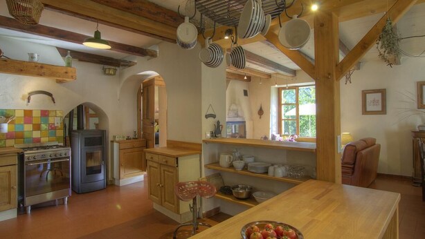 A rustic kitchen with wooden beams, a stove, and hanging pots. - Le Tilleret - Chezery-forens (CHEZERY-FORENS)