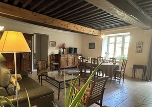 Un salon comprenant un canapé, une table à manger et des chaises. On y trouve également un téléviseur, un meuble et une fenêtre laissant entrer la lumière naturelle.