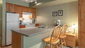 Une cuisine avec des meubles de rangement en bois, un réfrigérateur blanc, une cuisinière, un évier et deux tabourets de bar.