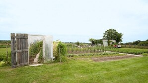 A garden with a wooden gate, a greenhouse, and a tractor in the background.
