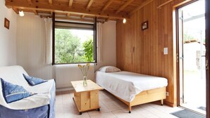 A room with a wooden ceiling, a bed, a sofa, a small table with a vase, and a window with curtains.