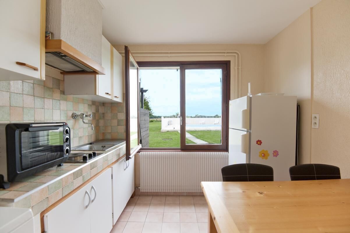 A compact kitchen with a built-in toaster, a window with a view of a house, and a white refrigerator.