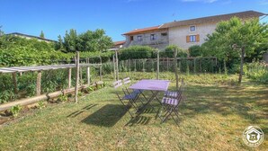 Un jardín con una mesa y sillas, una pérgola y una casa al fondo.