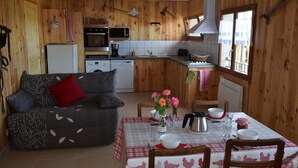 Una cocina acogedora de estilo cabaña con paredes de madera, una mesa de comedor dispuesta con vajilla y un sofá con un cojín rojo.