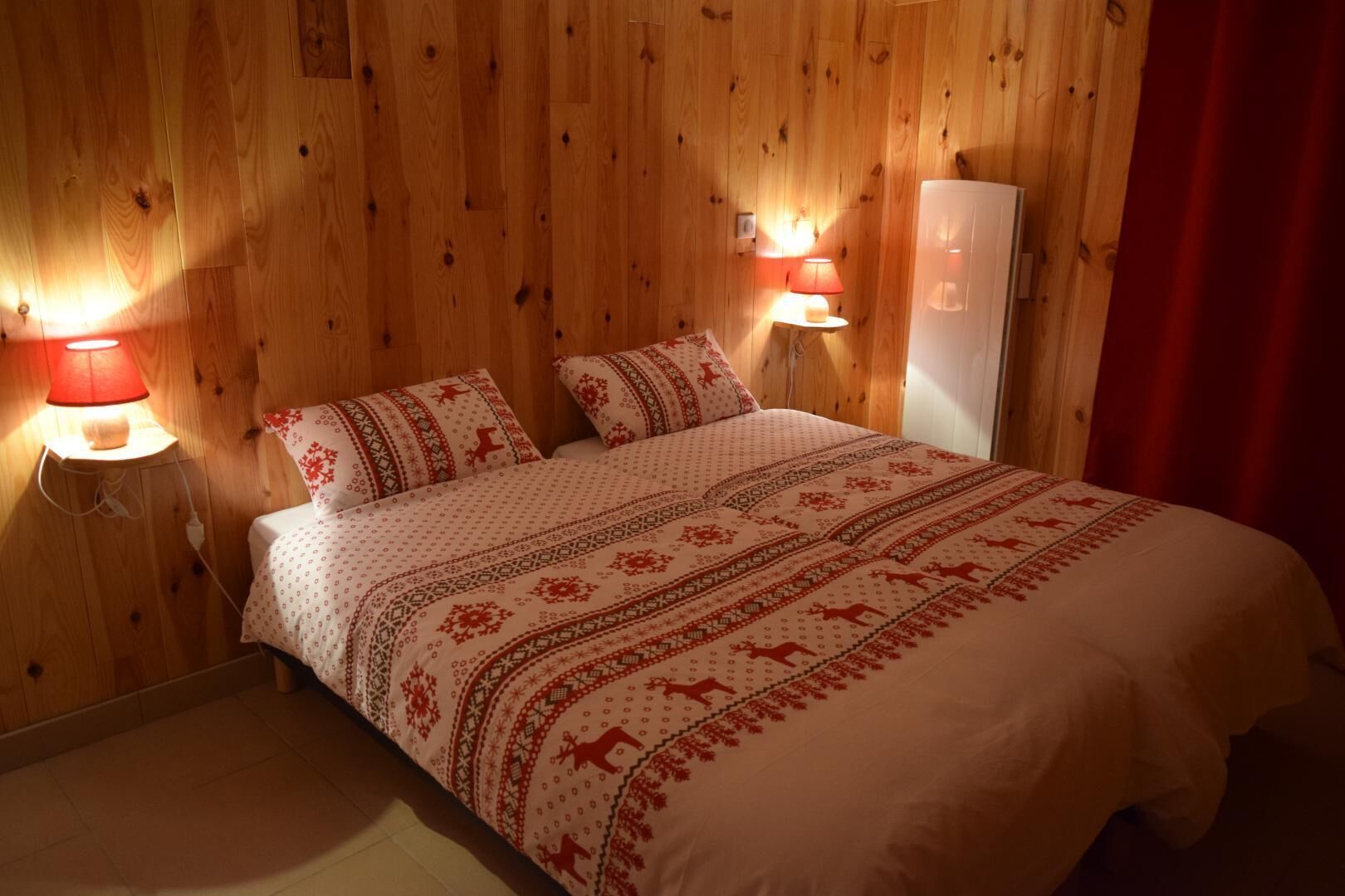 A cozy room with wooden walls, a bed with patterned bedding, two bedside lamps, and a red curtain.