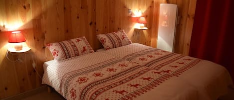 Een gezellige kamer met houten wanden, een bed met beddengoed met een patroon, twee bedlampen en een rood gordijn.