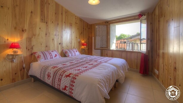 Dormitorio con paneles de madera, una cama, dos lámparas de noche y una ventana con vistas a edificios.