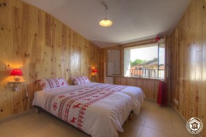 Dormitorio con paneles de madera, una cama, dos lámparas de noche y una ventana con vistas a edificios.