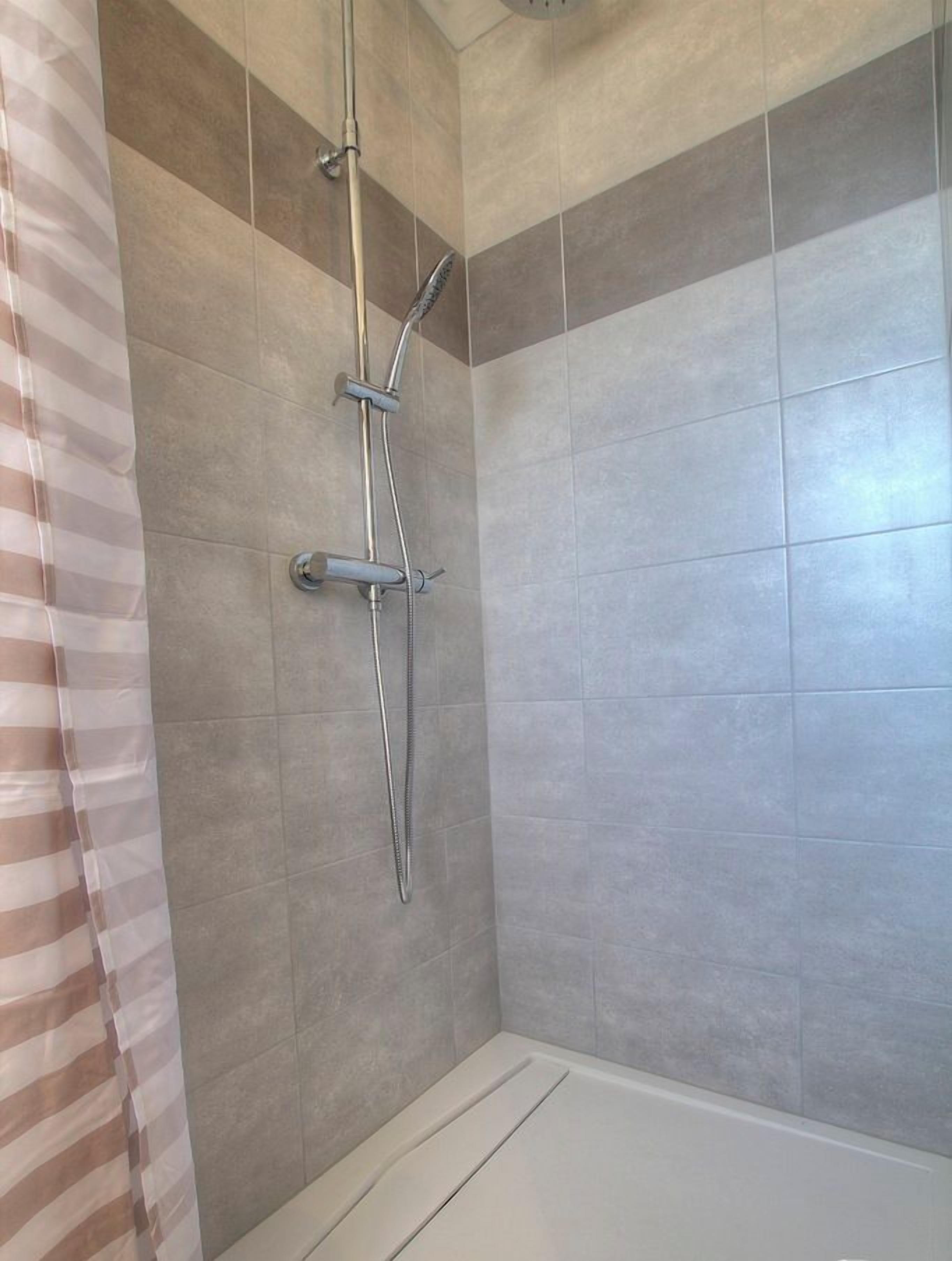 A shower with a handheld showerhead and a wall-mounted faucet.