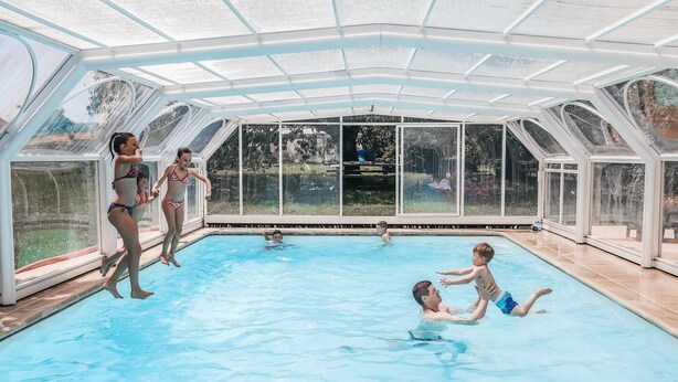 Ein beheiztes Hallenbecken mit Glasdach, umgeben von einer Poolterrasse.