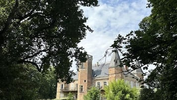 Un edifici gran i històric amb una torre destacada, envoltat de vegetació abundant i un jardí ben cuidat.