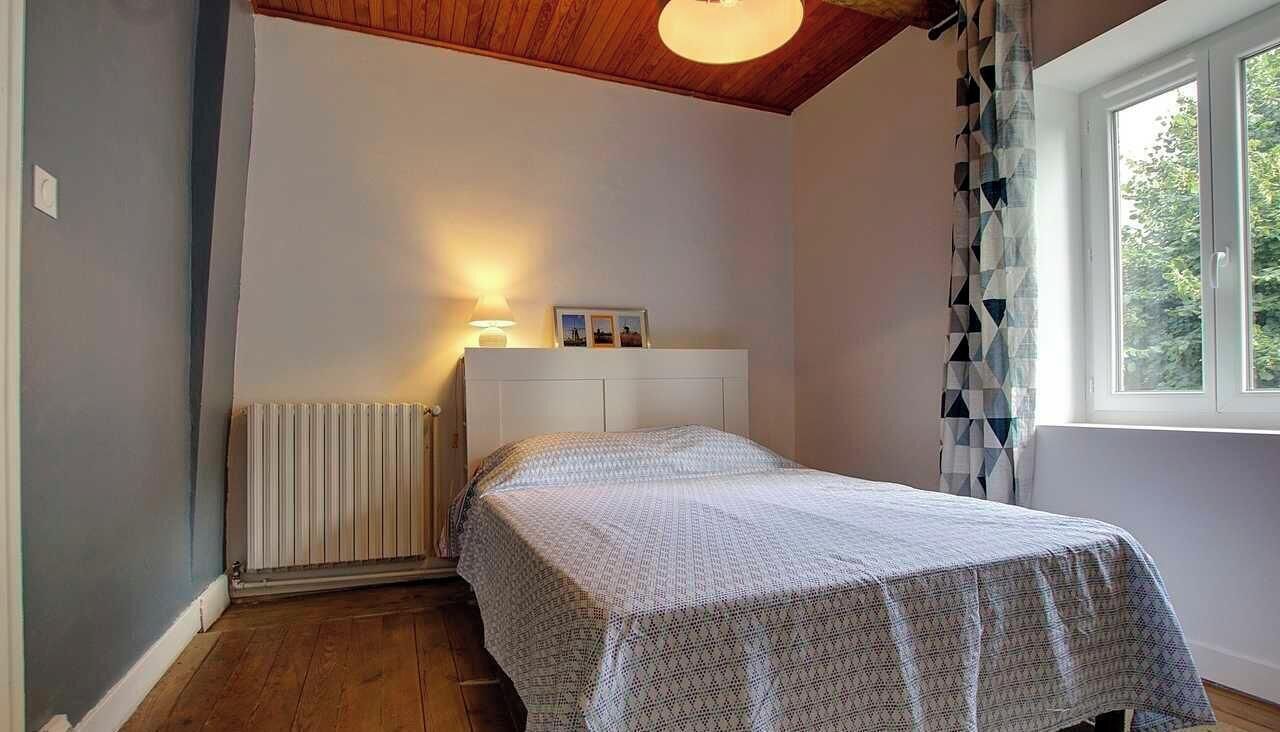 Una camera da letto con un letto, un termosifone, una finestra con tende e una luce a soffitto.