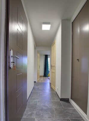 A hallway with a tiled floor, a door with a key lock, and a ceiling light.