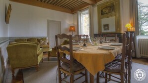 A dining room with a table set for four, wooden chairs, a chandelier, and a view of the outdoors through a window.