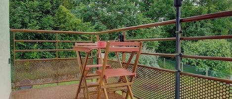 A balcony with a metal railing, a wooden table, and chairs.