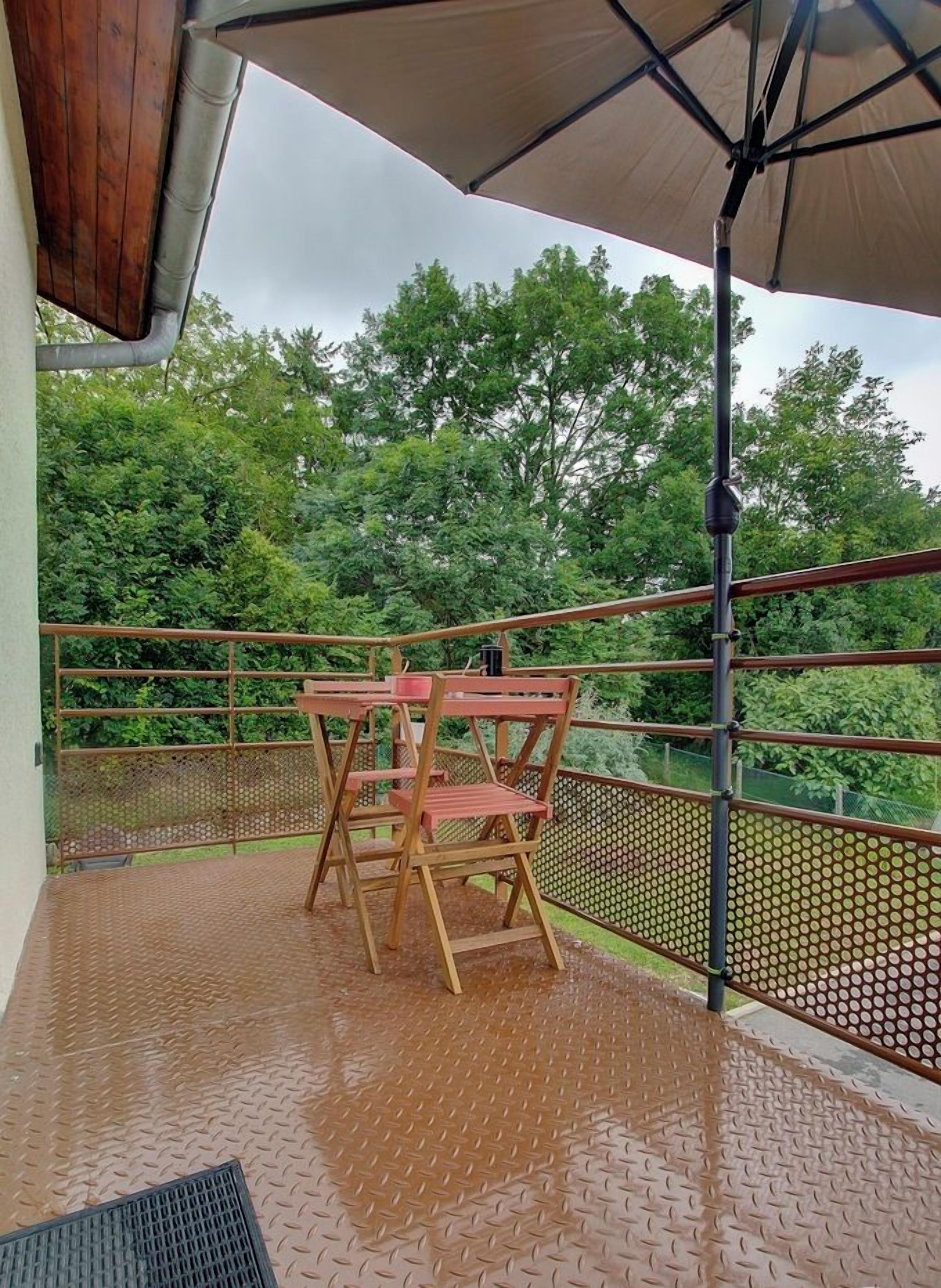 A balcony with a metal railing, a wooden table, and chairs.