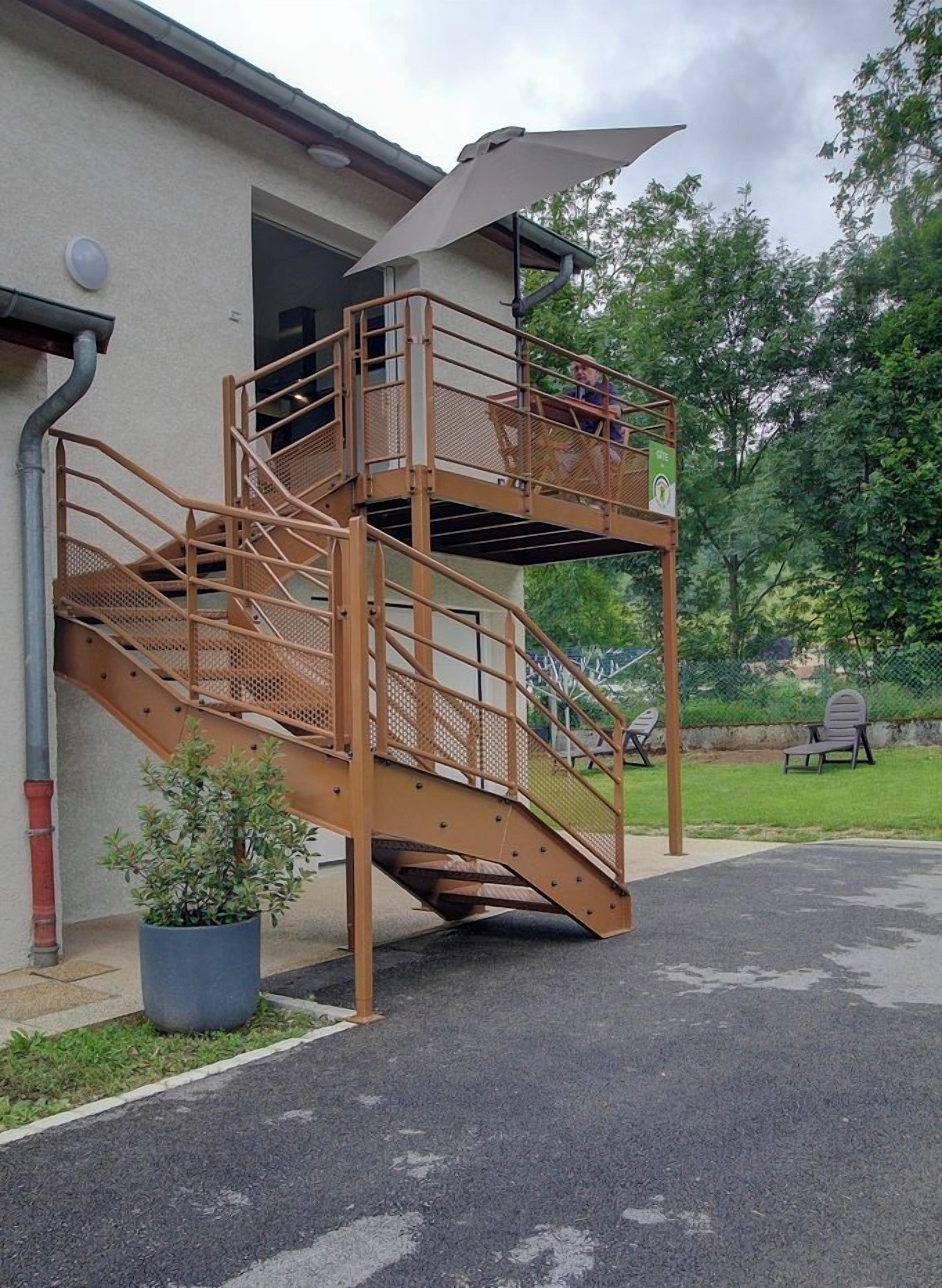 A multi-level outdoor staircase with a metal railing, a potted plant, and a picnic table in the background.