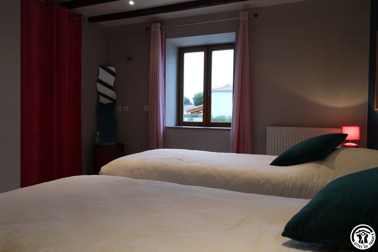A bedroom with two beds, a window with curtains, a radiator, and a red lamp.