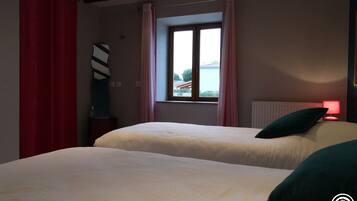 A bedroom with two beds, a window with curtains, a radiator, and a red lamp.
