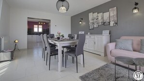 Une cuisine moderne avec des meubles blancs, une table à manger avec des chaises et un canapé rose dans l’espace salon.