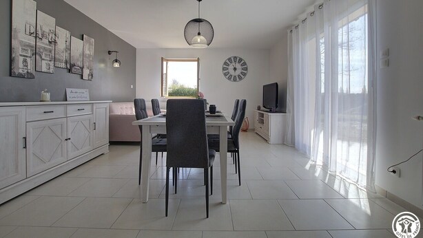 Un espace repas moderne avec une table blanche, des chaises grises, une suspension et une horloge au mur.