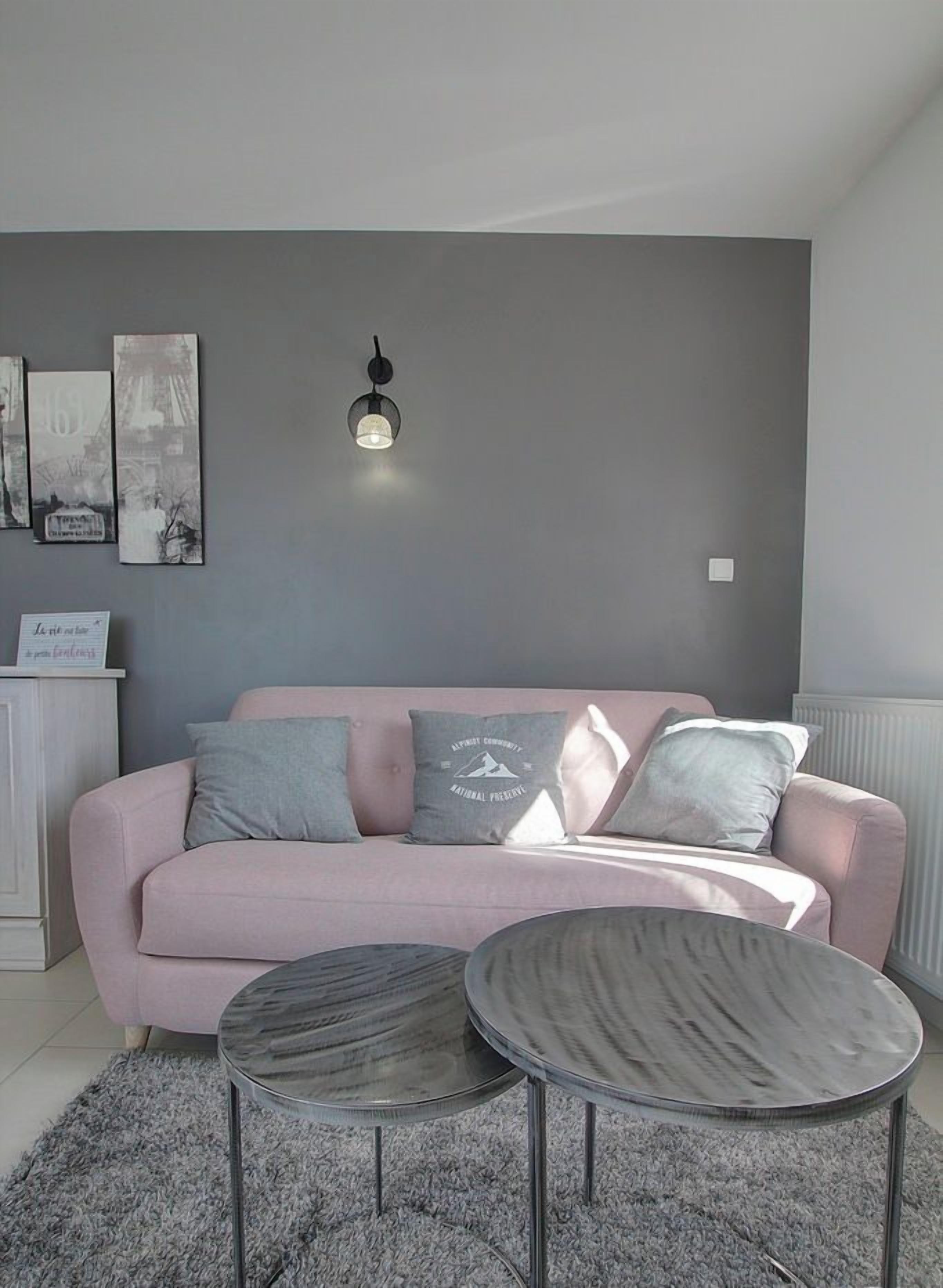 Ein modernes Wohnzimmer mit einem grauen Sofa, zwei runden Tischen und Wandbildern.