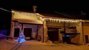Un edificio cubierto de nieve con fachada de piedra, un porche de madera y adornos de hielo.