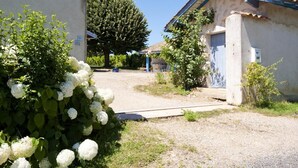 Un bâtiment à la façade en béton, doté d’un toit en métal et agrémenté d’un petit jardin où poussent des fleurs blanches.