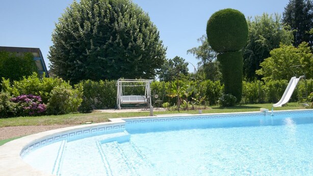 Une piscine avec un toboggan, entourée d’une végétation luxuriante et agrémentée d’une pergola.