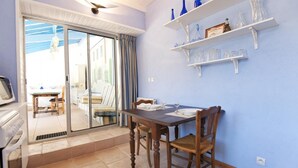 Un coin repas avec une table dressée pour quatre personnes, une porte-fenêtre coulissante donnant sur une terrasse extérieure et des étagères ornées d’objets décoratifs.