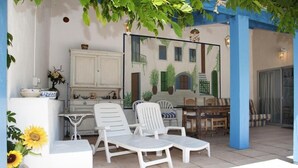 Un espace extérieur aménagé avec des meubles blancs, un buffet et une fresque représentant un bâtiment.
