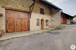 Un bâtiment en pierre doté de grandes portes de garage en bois, d’un petit porche et d’une antenne parabolique.