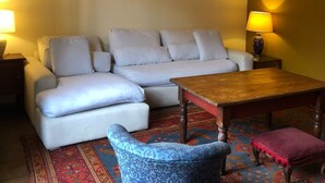 Uma sala de estar com sofá, mesa pequena, poltrona estampada e tapete.