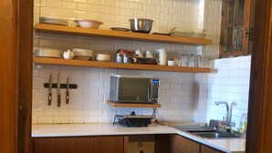Uma cozinha compacta com azulejos brancos tipo metrô, armários de madeira, pia de aço inoxidável e micro-ondas.