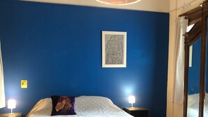 Quarto com uma cama grande, duas luminárias de cabeceira, uma obra de arte emoldurada na parede e piso de madeira.