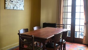 Uma sala de jantar com mesa e cadeiras de madeira, tapete estampado, luminária no teto e janela com cortinas.