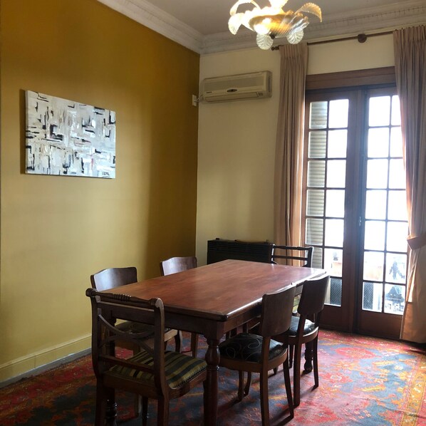 Un comedor con una mesa y sillas de madera, un tapete estampado, una lámpara en el techo y una ventana con cortinas.