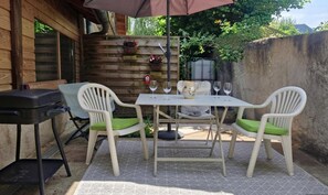 An outdoor patio with a table and chairs, a grill, and a wooden wall with planters.