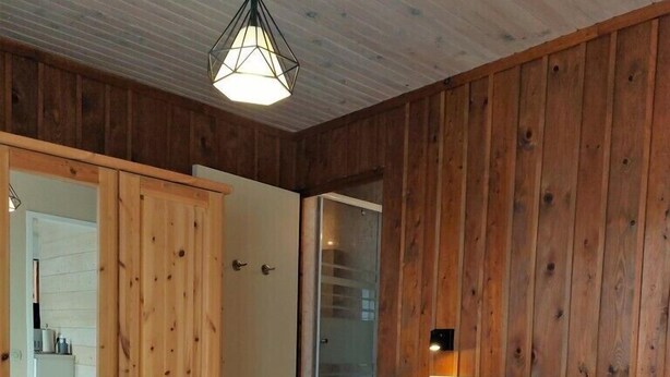 Ein Schlafzimmer mit einer Holzwand, einem großen Bett mit vielen Kissen, einem Holzschrank und einer Hängeleuchte.