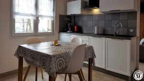 Eine kompakte Küche mit Esstisch, weißen Schränken, einer schwarzen Dunstabzugshaube und einem Fenster mit Milchglas.