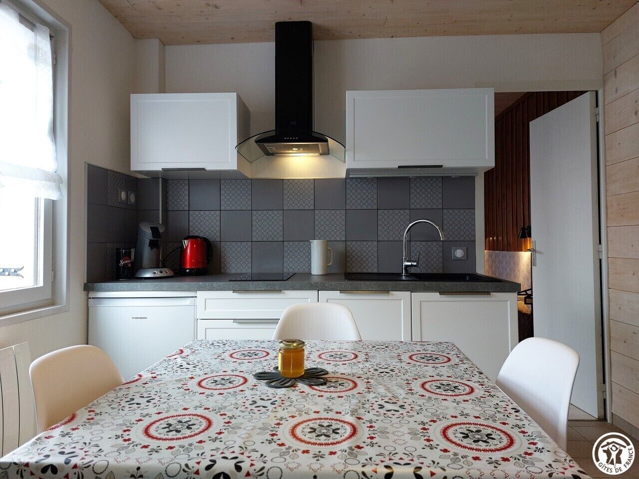 A compact kitchen with white cabinets, a black range hood, and a patterned tablecloth.