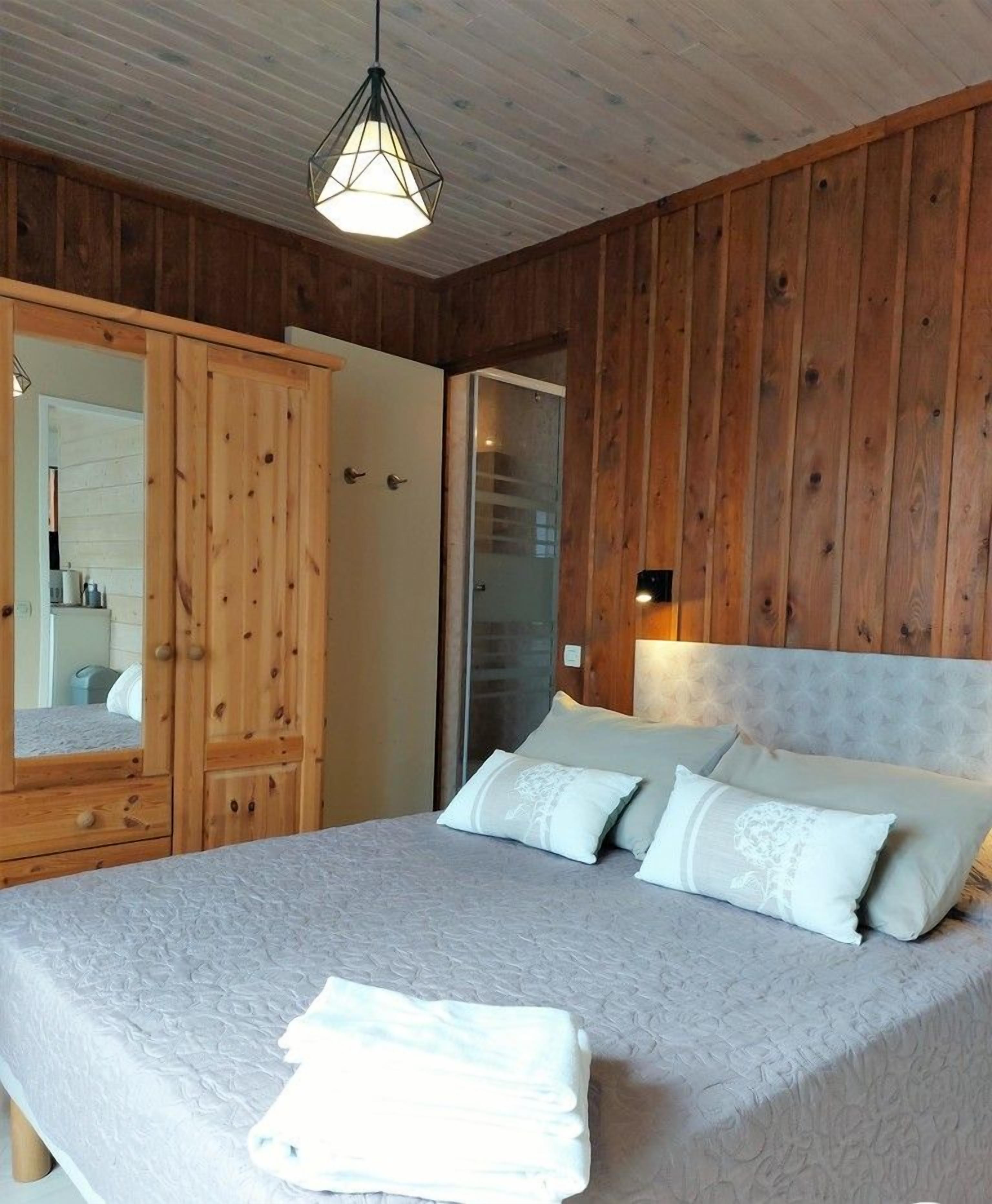 Ein Schlafzimmer mit einer Holzwand, einem großen Bett mit vielen Kissen, einem Holzschrank und einer Hängeleuchte.