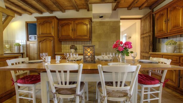 Una cocina de madera con sillas blancas, una mesa de comedor preparada para cuatro personas y un florero con flores.