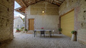 Un edificio rústico de piedra con piso de grava, una mesa de madera con sillas y una puerta de garaje amarilla.