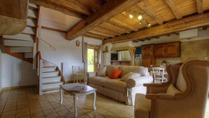 Amplia sala de estar con escalera de madera, un sofá color beige, una mesa de centro y una mesa de comedor con sillas.