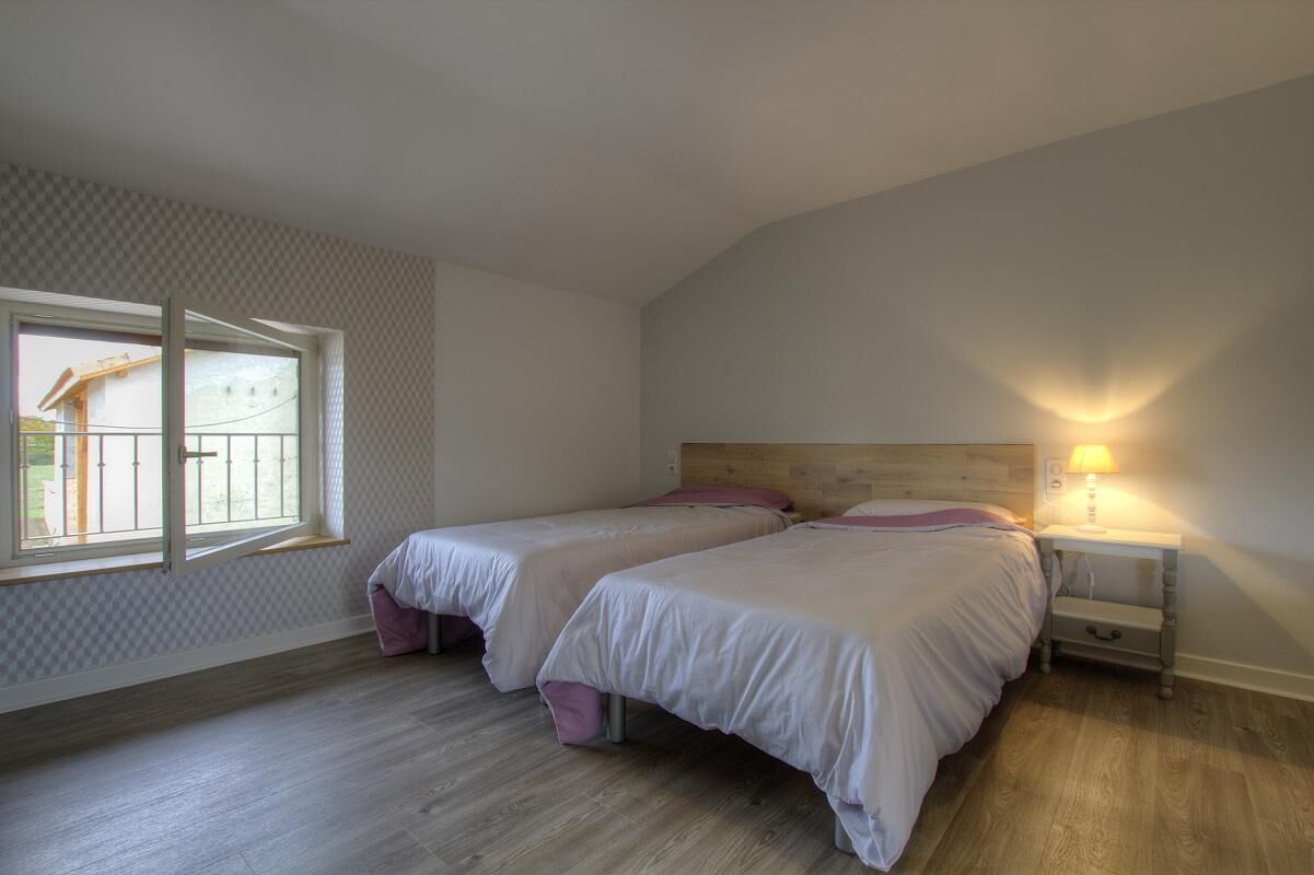 Een slaapkamer met twee bedden, een raam en een nachtkastje met een lamp.